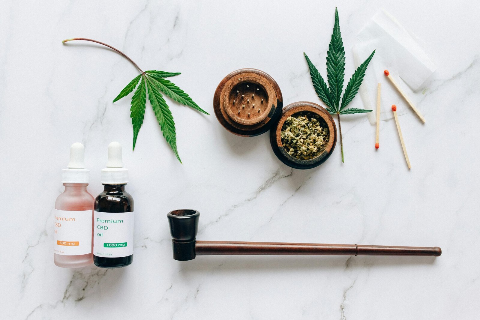 Top view of cannabis products including CBD oils, leaves, and smoking accessories on a marble surface.