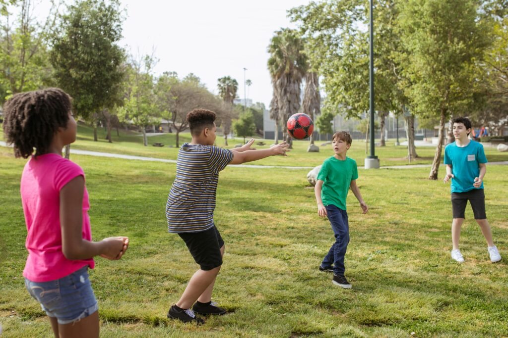 A diverse group of kids enjoying ball games outdoors in a sunny park setting.