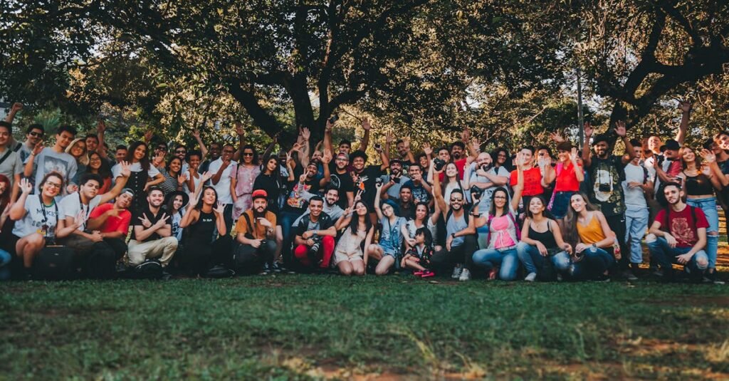 A diverse group of people gathering outdoors in a park, celebrating together with raised hands.
