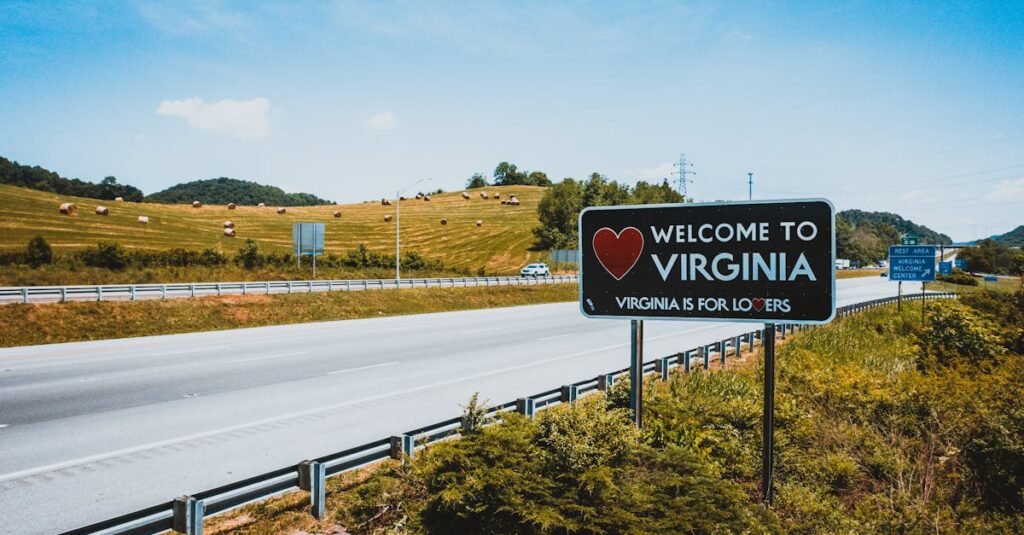 Empty asphalt highway in hilly countryside near road sign with welcome to Virginia inscription on sunny day
